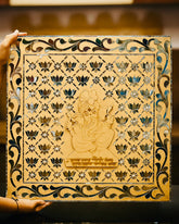 Decorative panel with intricate carvings of a deity and floral patterns, held by a hand.