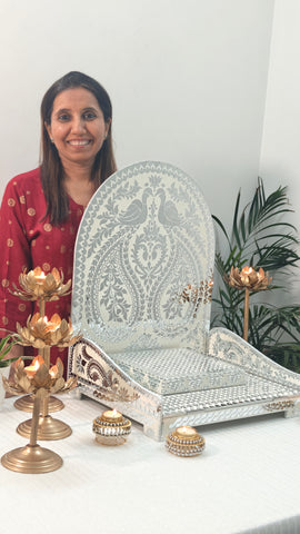 Woman showcasing decorative white mirror mosaic chowki with peacock floral design, elegant pooja setup with lotus candle holders for festive home temple décor.
